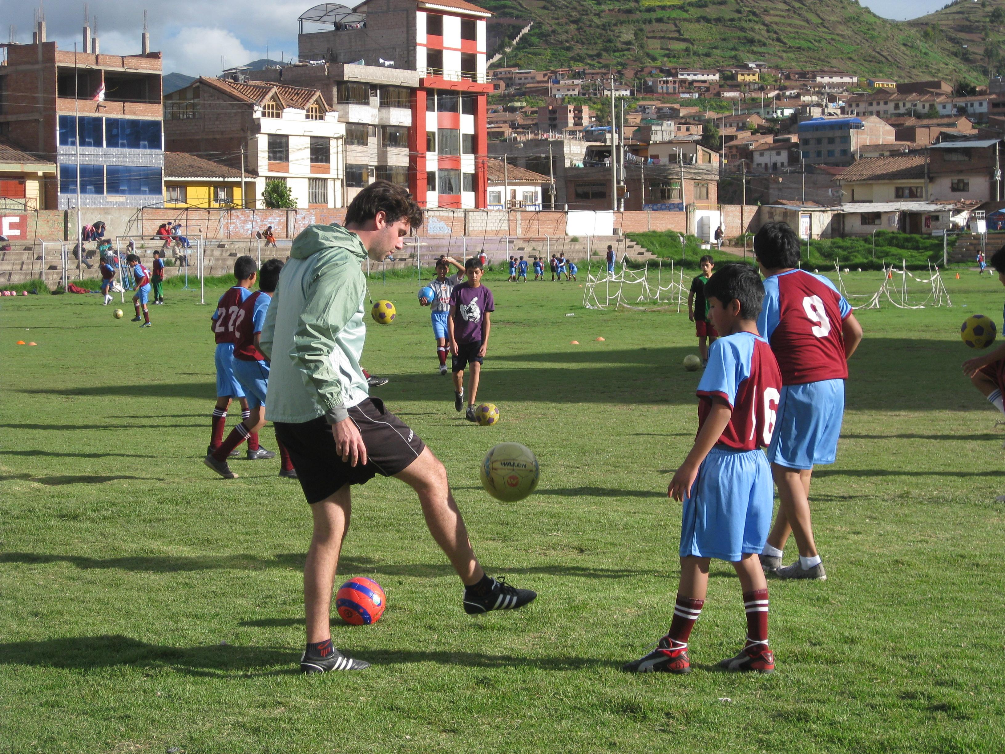 A man volunteers as a sports coach in Peru and teaches children the basics of football A Projects Abroad volunteer gets hands-on coaching experience in Peru working with school children
